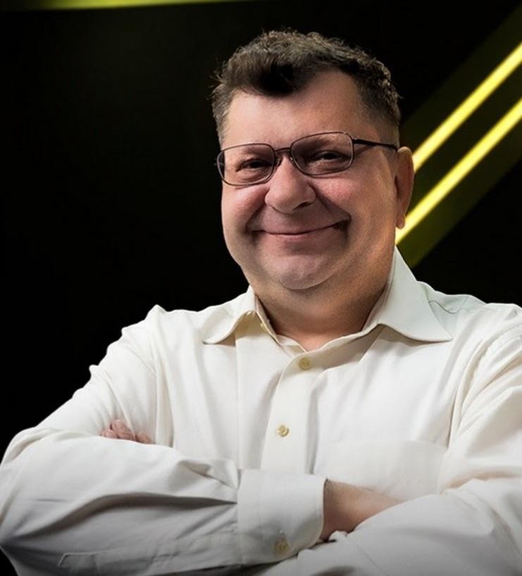 Zbigniew Ryszard Stonoga gestykulujący podczas publicznego wystąpienia, z rozmytym tłem sugerującym wydarzenie lub transmisję online, oddający jego zaangażowanie i bezpośredniość.