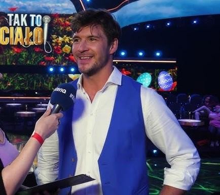 Mikołaj Roznerski w naturalnej interakcji z fanami lub na planie filmowym, ukazujący jego charyzmę.