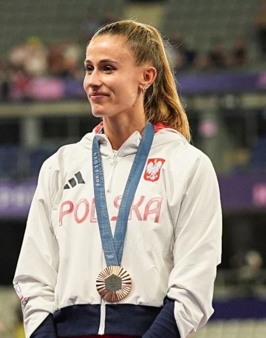 Alt: Natalia Bukowiecka i Konrad Bukowiecki, polska para sportowców, uśmiechnięci i zrelaksowani w swobodnej scenerii, symbolizujący ich wspólne życie i wsparcie.