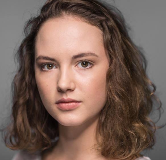 Martyna Byczkowska śmiejąca się szczerze na planie filmowym, w tle zamazane elementy produkcji, ukazująca radość i autentyczność.