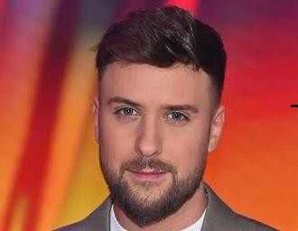 Aleksander Tomasz Sikora uśmiechnięty, w zbliżeniu, rozmawia z kimś w studiu telewizyjnym.