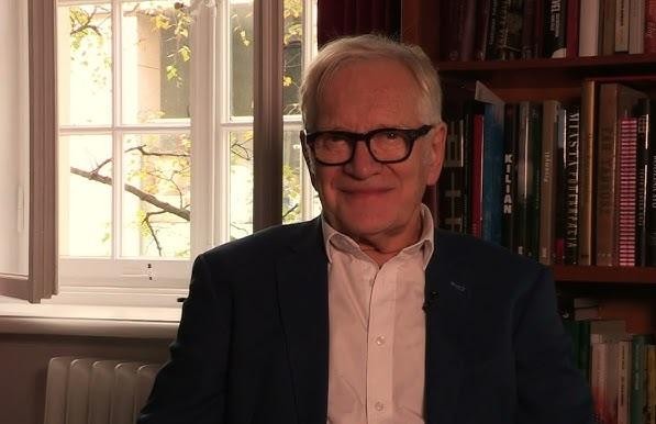 Andrzej Seweryn na scenie teatralnej, w trakcie dynamicznego występu, w czarno-białym ujęciu, z teatralnym oświetleniem.