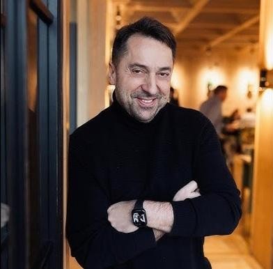 Marcin Miller w stylowym stroju, pozujący obok luksusowego czerwonego Mercedesa Cabrio lub Lexusa, symbolizujący jego pasję do motoryzacji i sukces.
