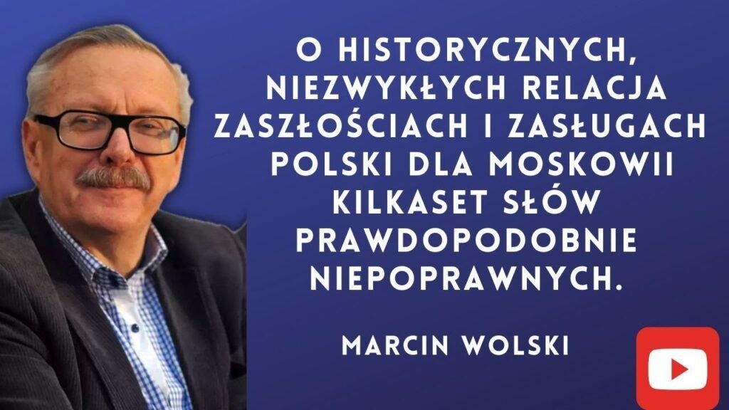Marcin Wolski w trakcie wystąpienia publicznego, uśmiechnięty i gestykulujący, na tle rozmytej sceny lub studia.