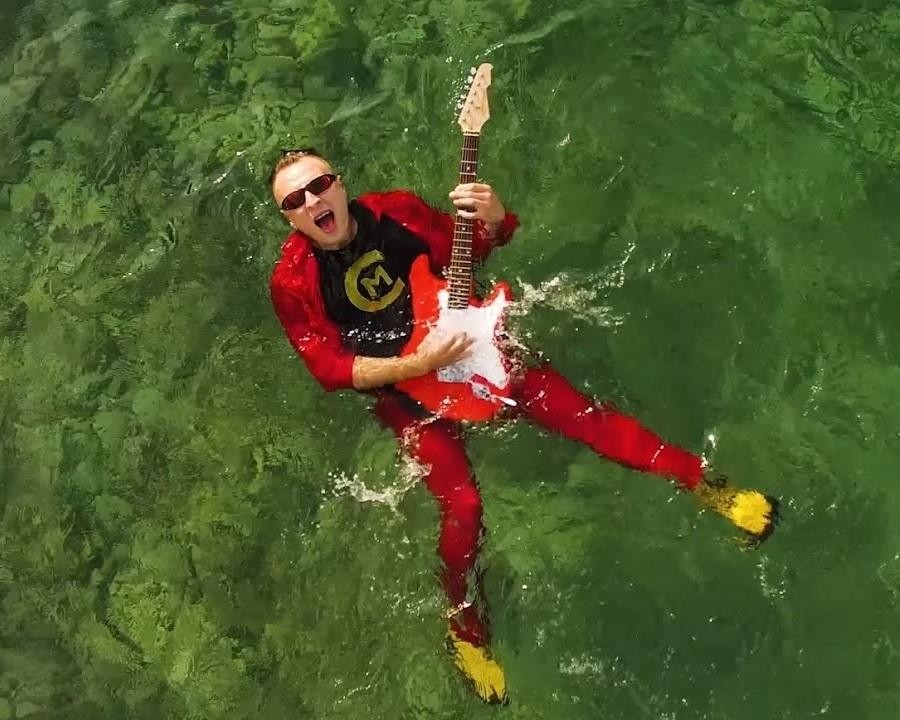 Czadoman (Paweł Dudek) na scenie podczas występu, z mikrofonem w dłoni, uśmiechnięty i pełen energii, w otoczeniu kolorowych świateł scenicznych.