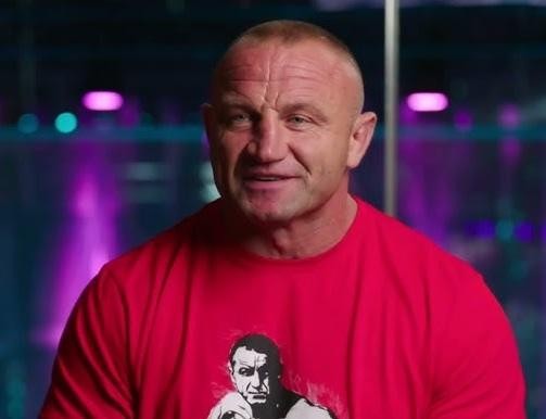 Mariusz Pudzianowski uśmiechnięty, w swobodnej pozie, podczas interakcji z fanami.