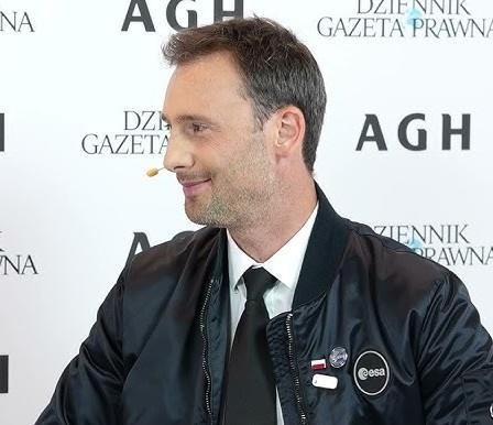 Sławosz Uznański, polski astronauta, trzymający smartfon i uśmiechający się do kamery, symbolizujący jego aktywność na Instagramie.